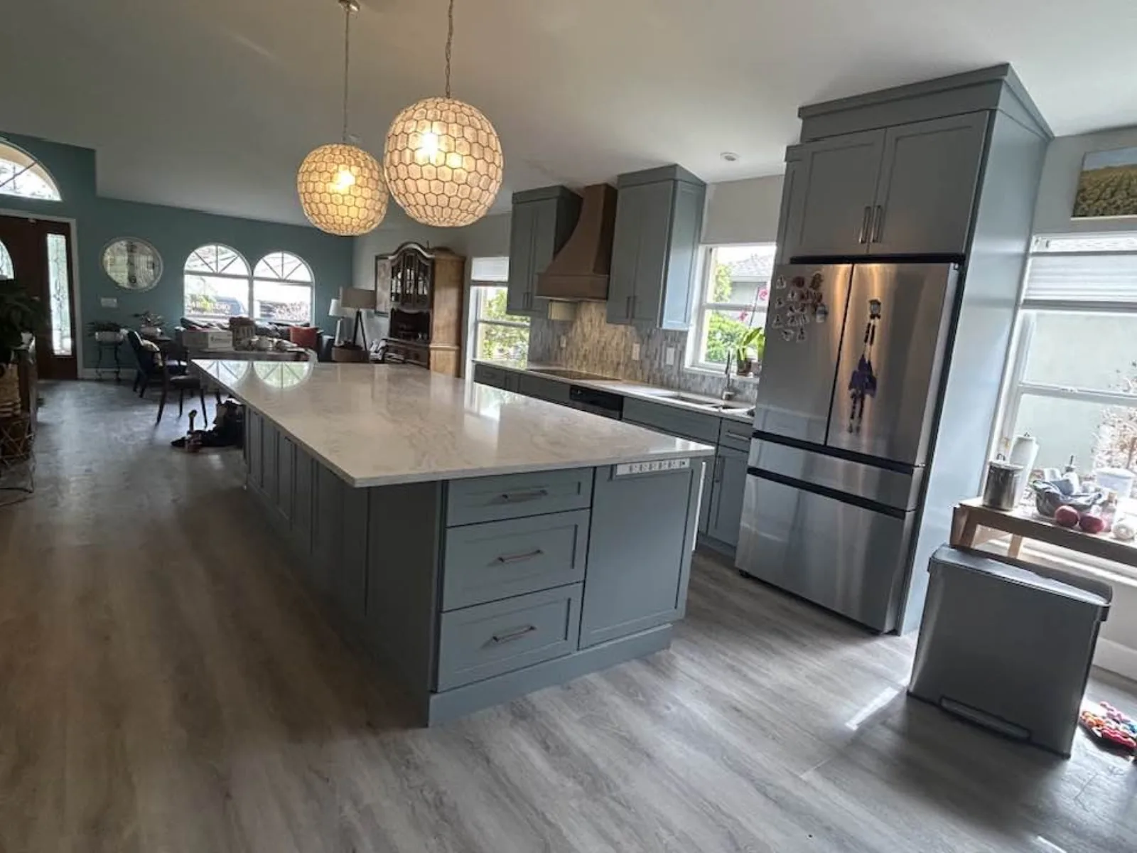Long gray island with woven pendant lights and stainless refrigerator